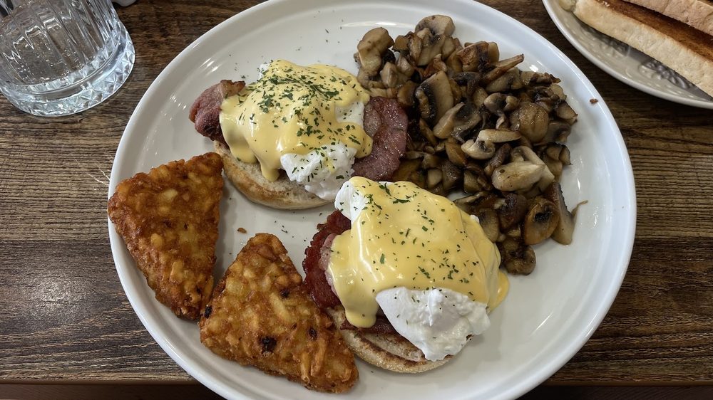 A wide table at Moonstone Cafe with eggs Benedict, hash browns, mushrooms, glasses and cutlery