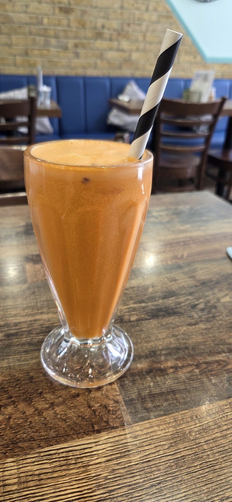 Orange milkshake in a footed glass with a striped straw
